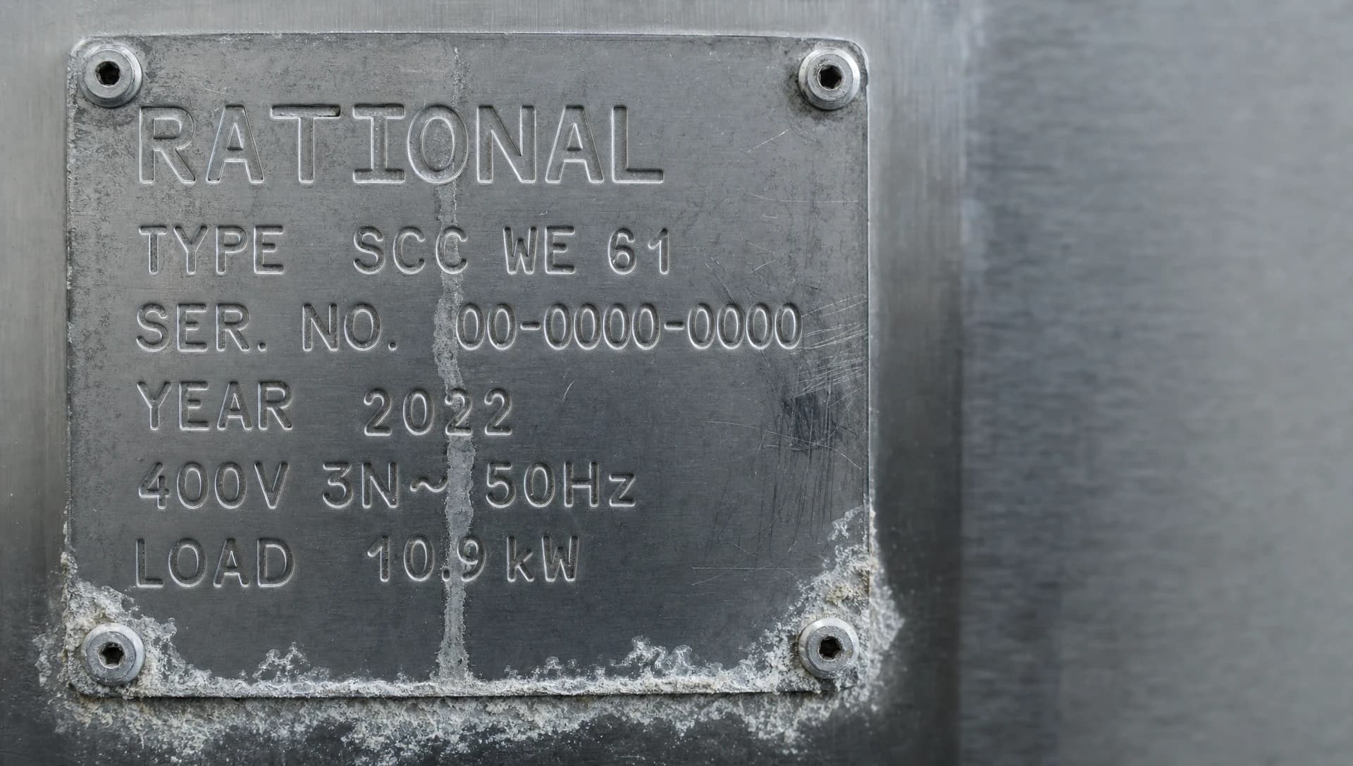 Macro photograph of the stamped stainless data plate on a Rational combi oven showing brand, model, serial and year.