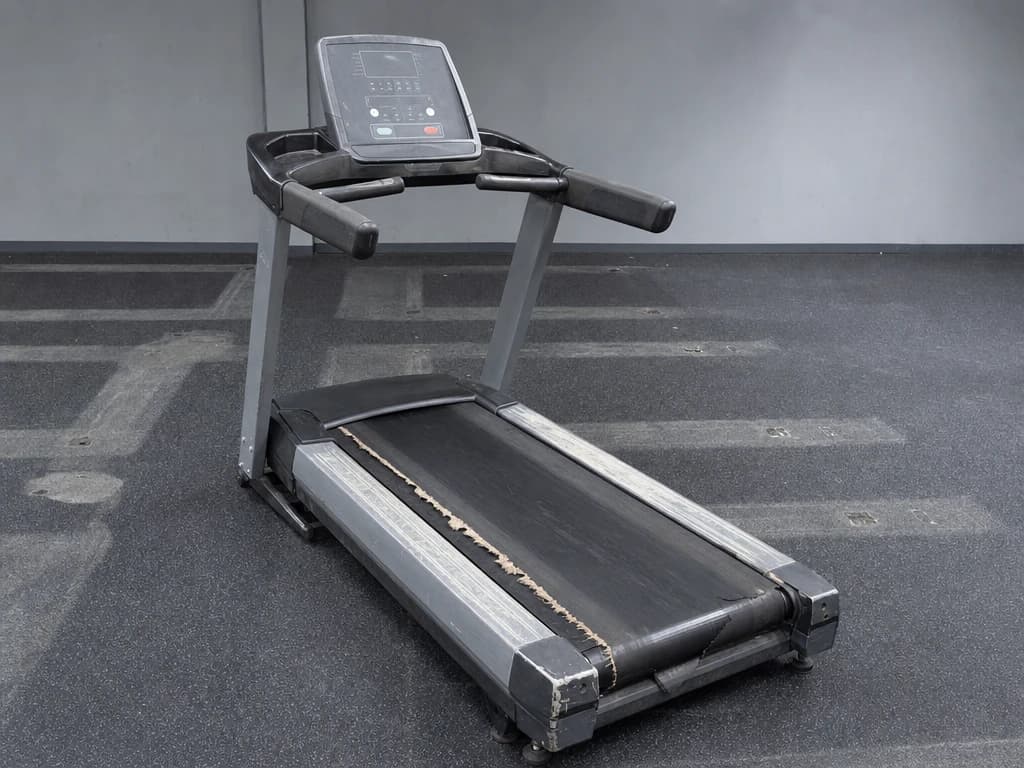 Life Fitness Integrity Series treadmill on a stripped gym floor, console dark, side rails scuffed.